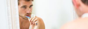 man brushing teeth in mirror