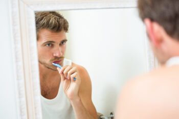 man brushing teeth in mirror