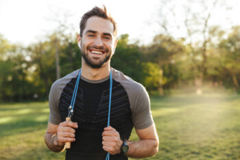 Man posing outdoors holding jumprope behind neck