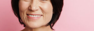Mature brunette woman smiling and looking at camera isolated over pink background